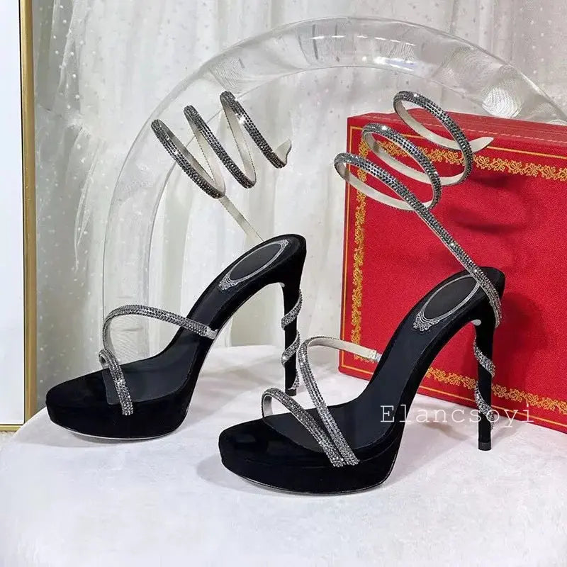 Top-down view of crystal-encrusted stiletto heels on a reflective surface.