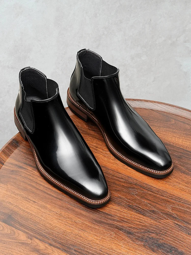 Black glossy leather Chelsea boots with elastic side panels and thick cushioned sole on white background