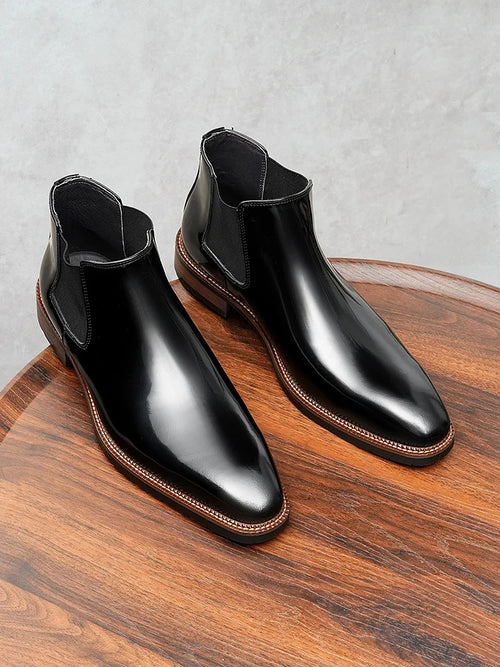 Black glossy leather Chelsea boots with elastic side panels and thick cushioned sole on white background