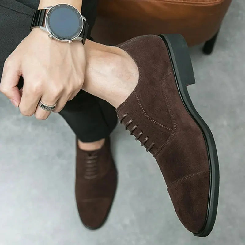 Elegant brown suede oxfords displayed on a polished surface, highlighting their sophisticated silhouette.